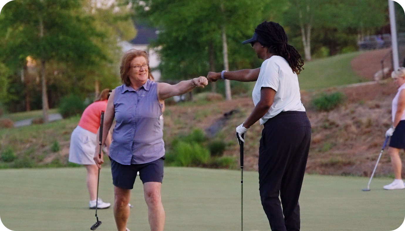 Two women fist-bumping on the green during an Op 36 adult class
