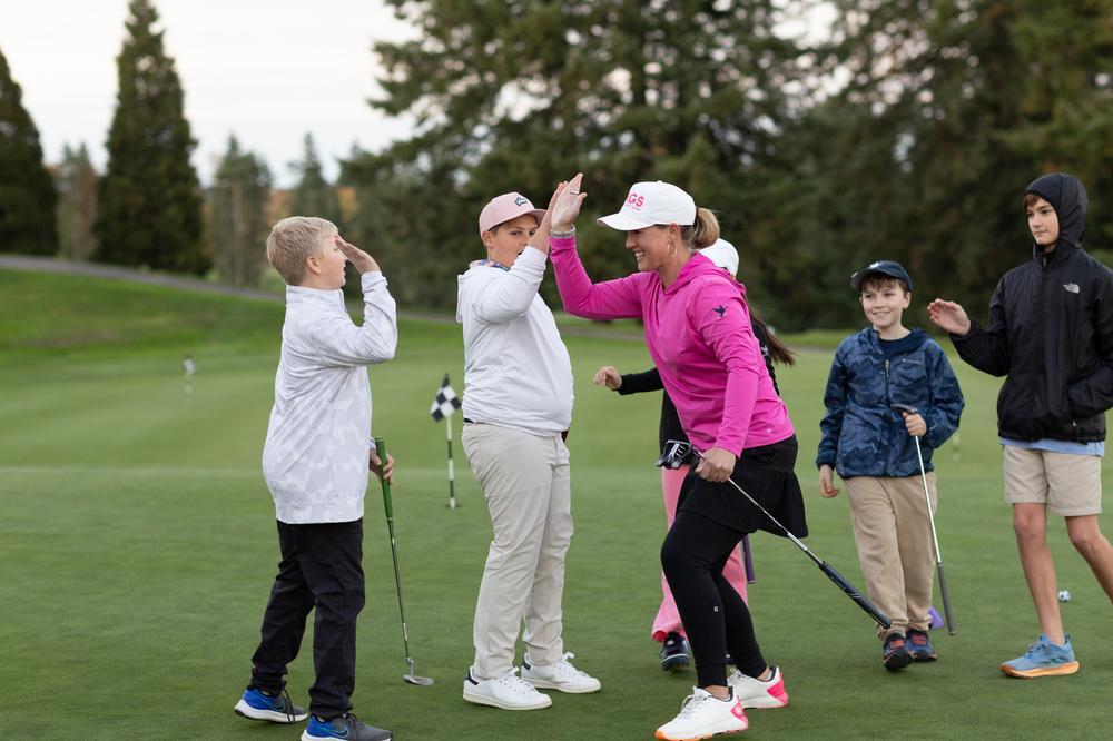 An Op 36 coach high-fiving junior golfers on the putting green