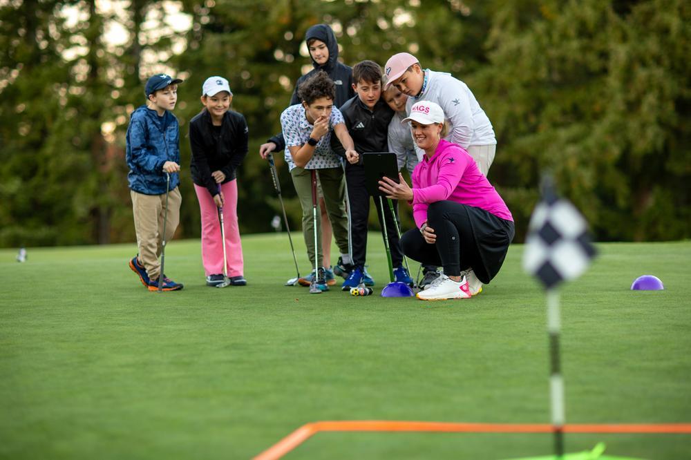 An Op 36 coach showing a group of juniors their progress on a tablet on the putting green