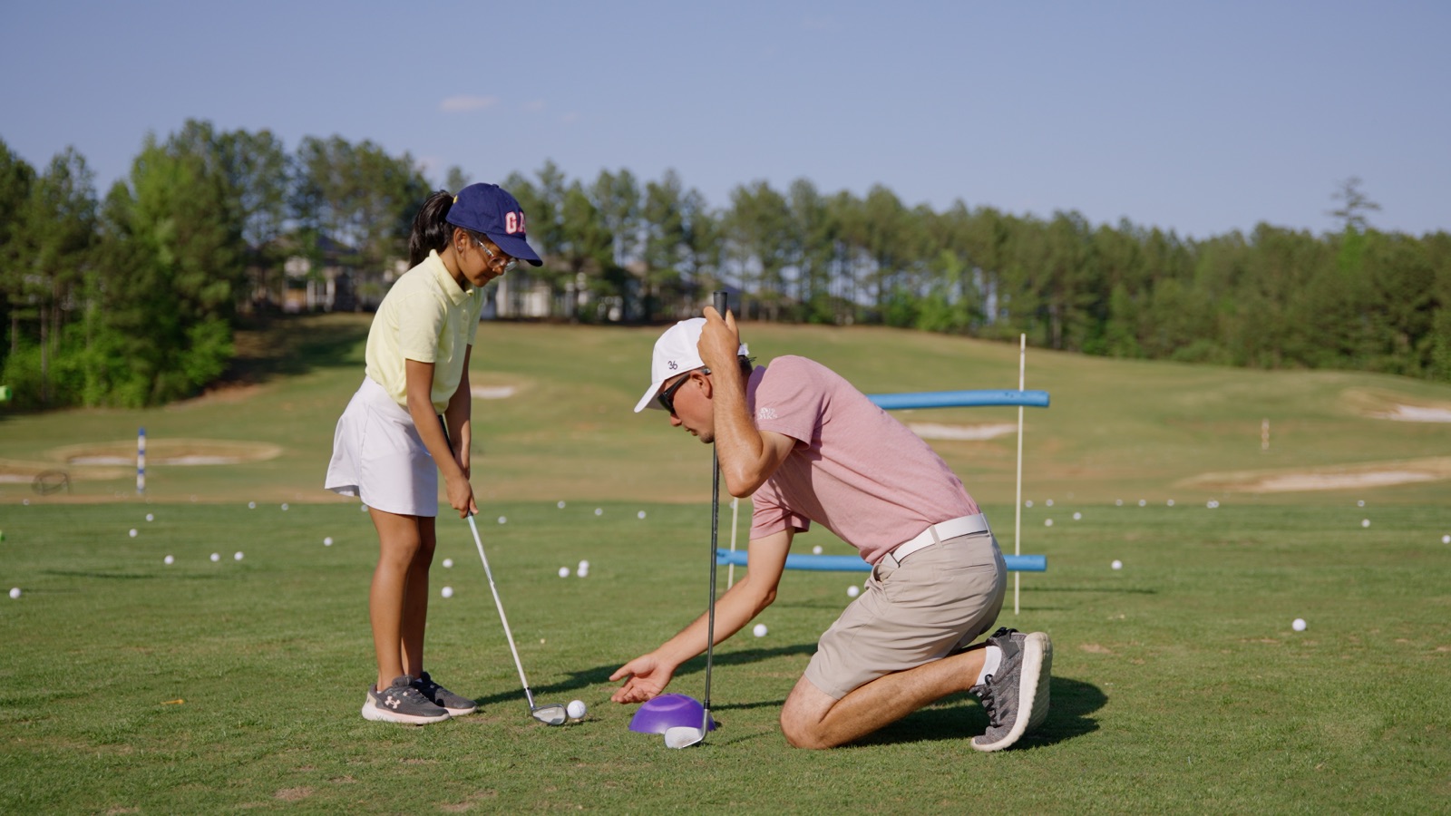 An Op 36 coach kneeling beside a junior golfer during a lesson on the range